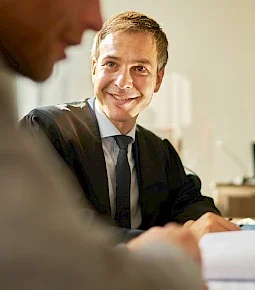 Ein Rechtsanwalt in Robe und Anzug lächelt während eines Gesprächs mit einem Klienten.