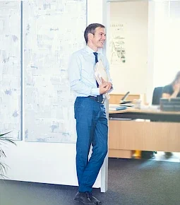 Mann in einem Büro, der an einer Wand steht und Unterlagen in der Hand hält.