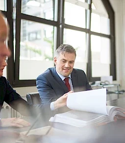 Mann in einem Anzug, der Dokumente während eines Meetings am Tisch betrachtet.