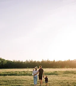 Eine Familie mit zwei Kindern, die Hand in Hand auf einem Feld spaziert.