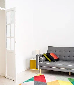 Grau gepolstertes Sofa mit bunten Kissen in einem hellen Raum mit einem bunten Teppich.