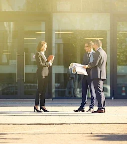 Drei Personen in Anzügen und eine Person in einem Kostüm führen ein Gespräch im Freien.